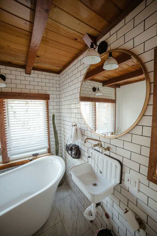 A white sink is mounted on a wall with a round mirror above it.