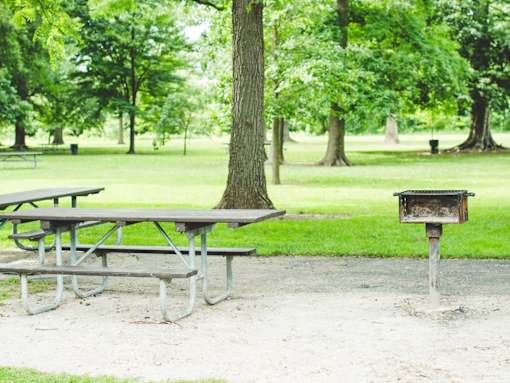 two picnic tables and a grill in a park