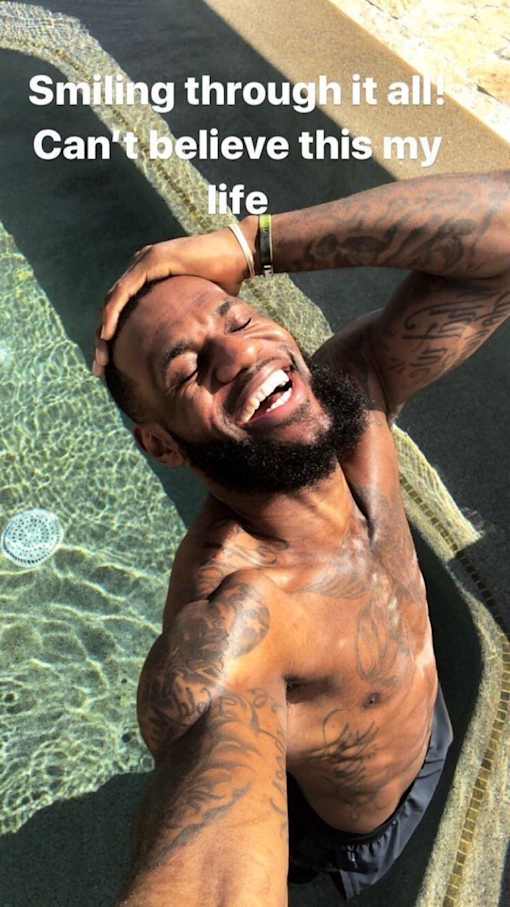 A man with tattoos on his arms is smiling and leaning on a pool edge.