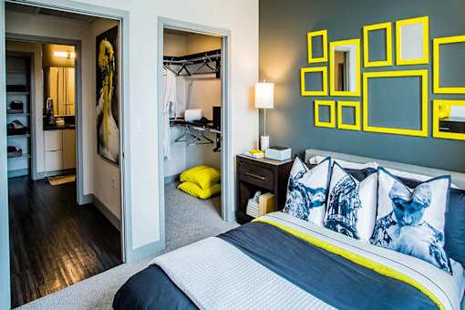 a bedroom with a bed with blue and yellow pillows   and a bathroom