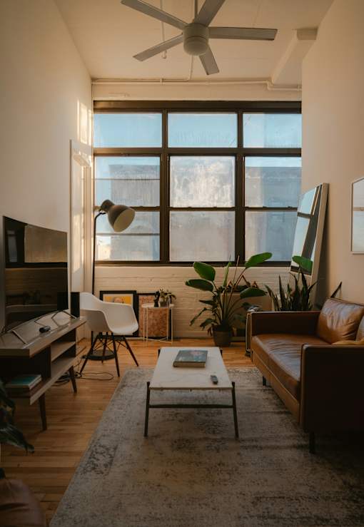 A living room with a brown couch, a white chair, a coffee table, and a large window.