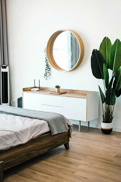 A bedroom with a bed, a mirror, and a plant.