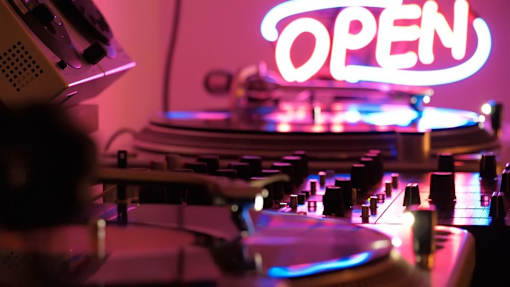A neon sign that says "OPEN" is lit up in a room with a DJ mixer.