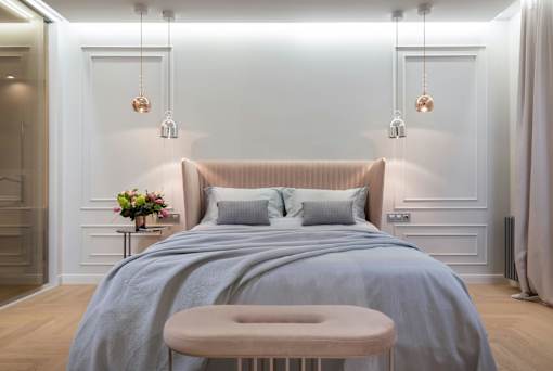 A bedroom with a bed, a small table with a vase of flowers, and a bench.