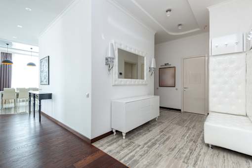 A white couch sits in a room with wood flooring and a large mirror above it.