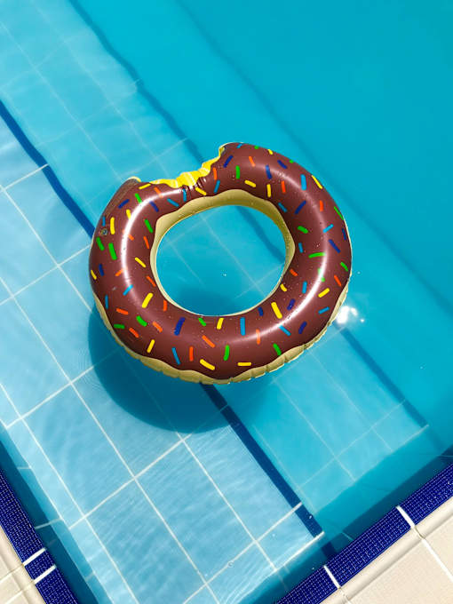 A chocolate donut with sprinkles is floating in a pool.