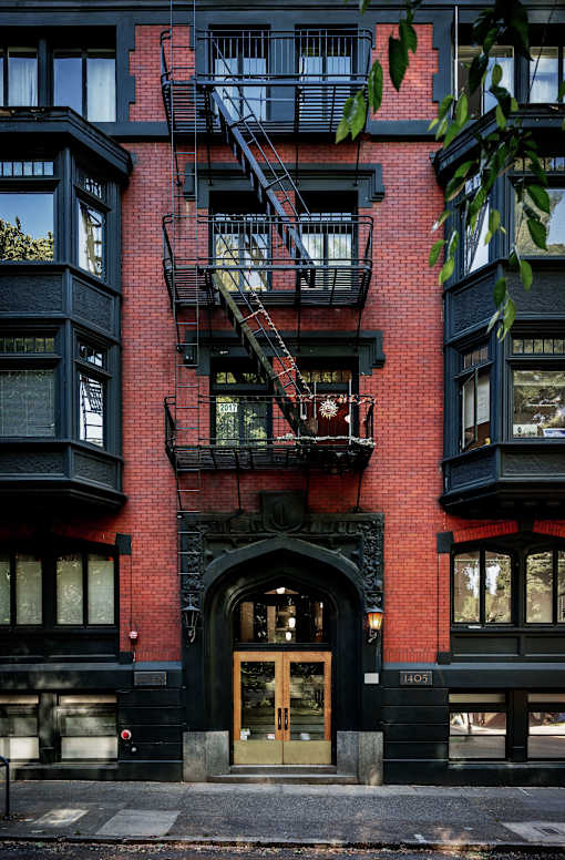 A red brick building with a black door and a fire escape.