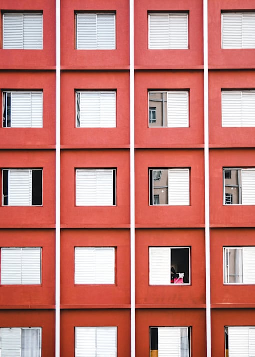 A red building with white window blinds and a few windows with curtains.