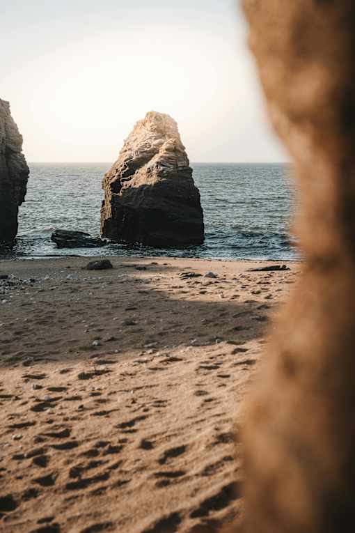 A beach scene with a large rock formation in the water.