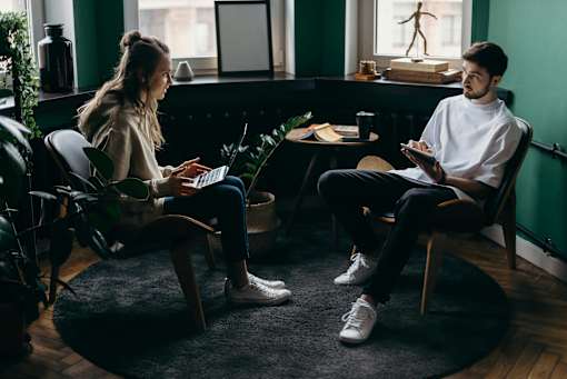 Two people sitting in a room with a laptop and a tablet.