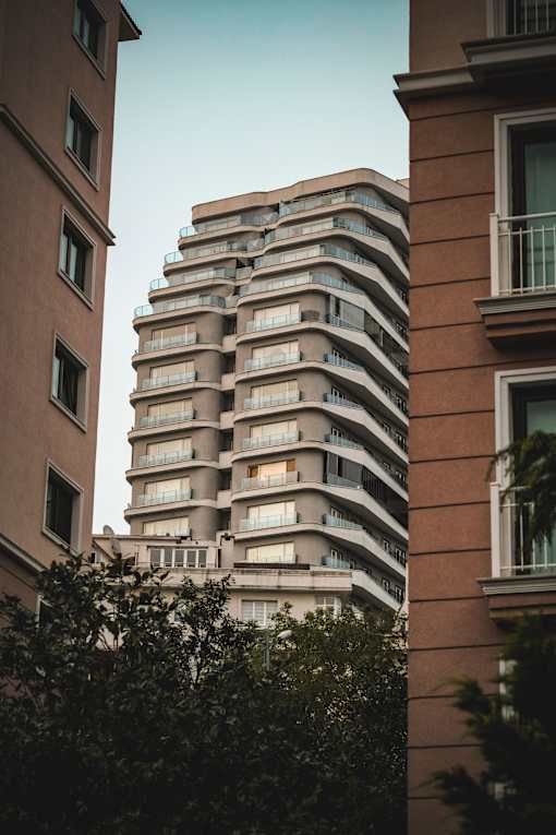 A tall building with balconies is seen between two shorter buildings.