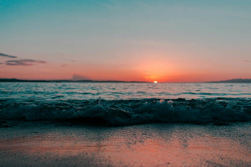 A beautiful beach scene with the sun setting over the ocean.