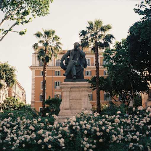 A statue of a seated man is surrounded by white flowers and palm trees.