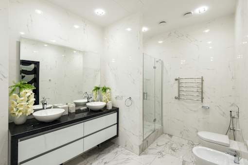 A bathroom with a marble wall and a black vanity with three sinks.