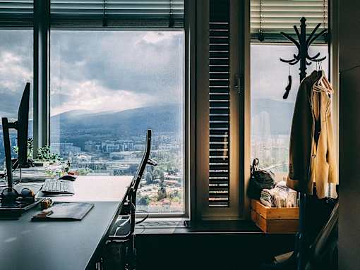 A room with a desk, chair, and a window overlooking a cityscape.
