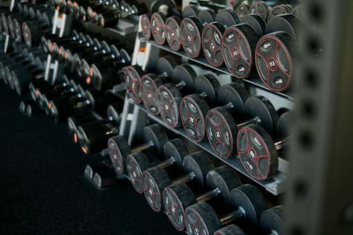 A row of black dumbbells with red and white weight plates are lined up on a rack.