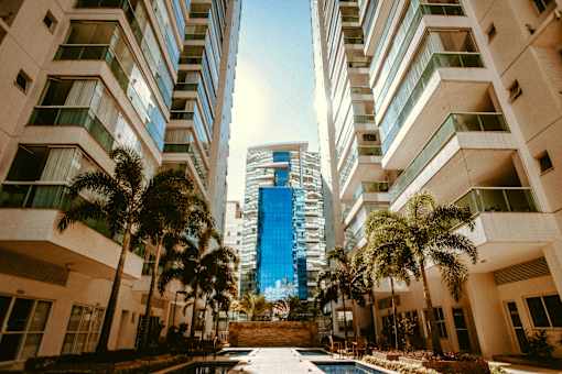 A tall building stands between two low-rise buildings with palm trees in the foreground.