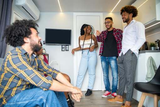 Four people are standing in a room with a television and a chair.