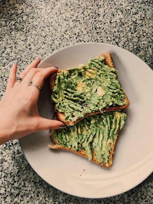 a hand holding a piece of toast with avocado on it