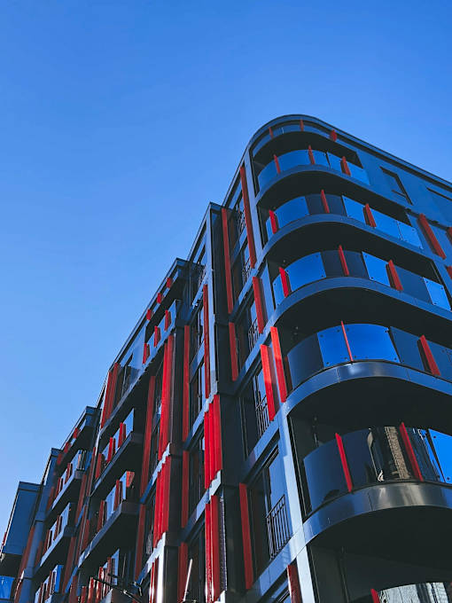 A tall building with red and blue balconies against a blue sky.