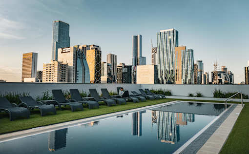 A pool with chairs and buildings in the background.