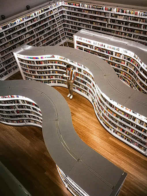 A person is standing in a library with a curved bookshelf.