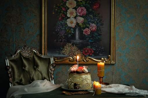 a cake with a candle on a table with a painting in the background