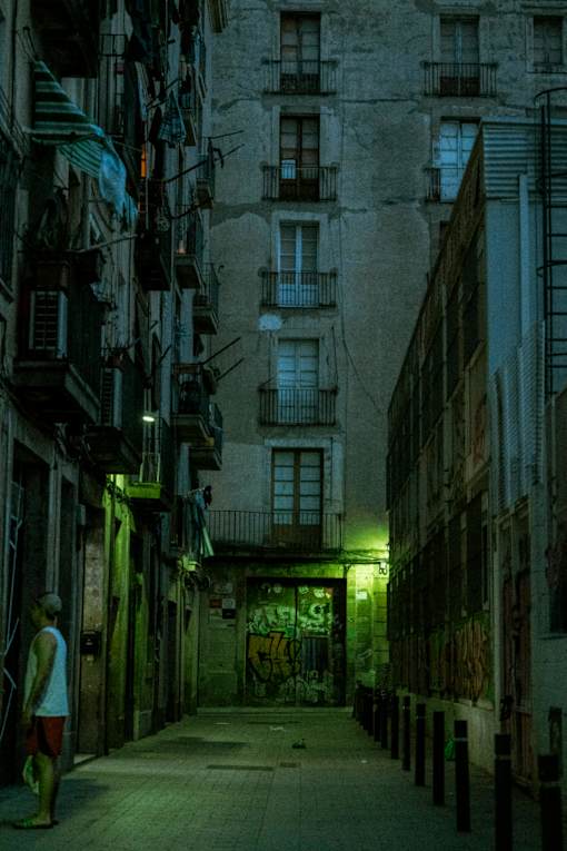 A man is standing on a narrow street between buildings.