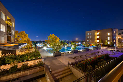 A pool area at night with lights on and buildings in the background.