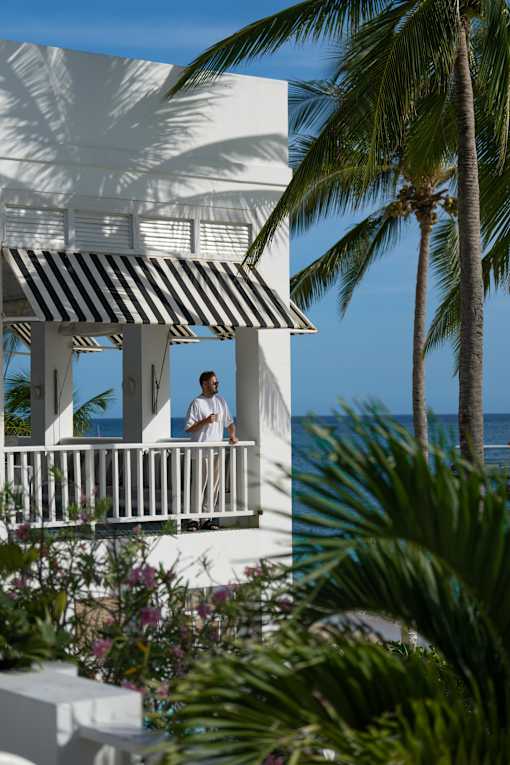 A man stands on a balcony overlooking the ocean.