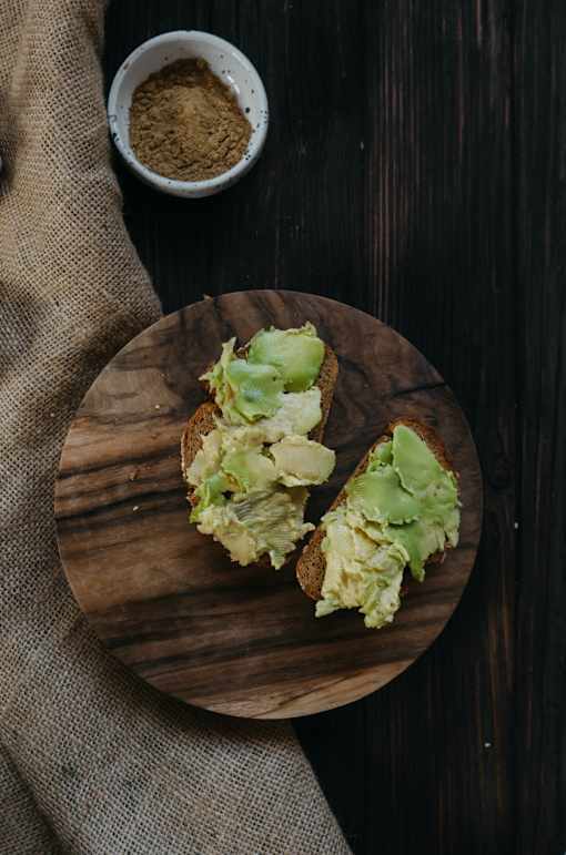 a picture of avocado toast on a wooden cutting board with a bowl of cocoa powder and a