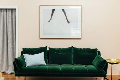 A green couch with a white pillow and a picture of a leg above it.
