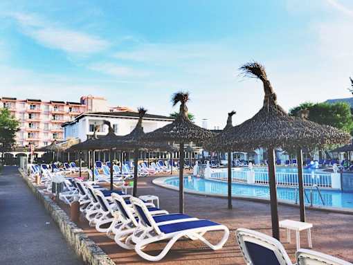 A row of sun loungers are arranged on a terrace next to a pool.