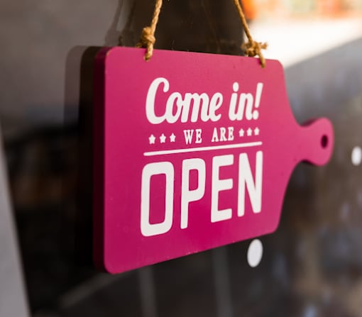 A pink sign that says "Come in! We are open" is hanging on a rope.