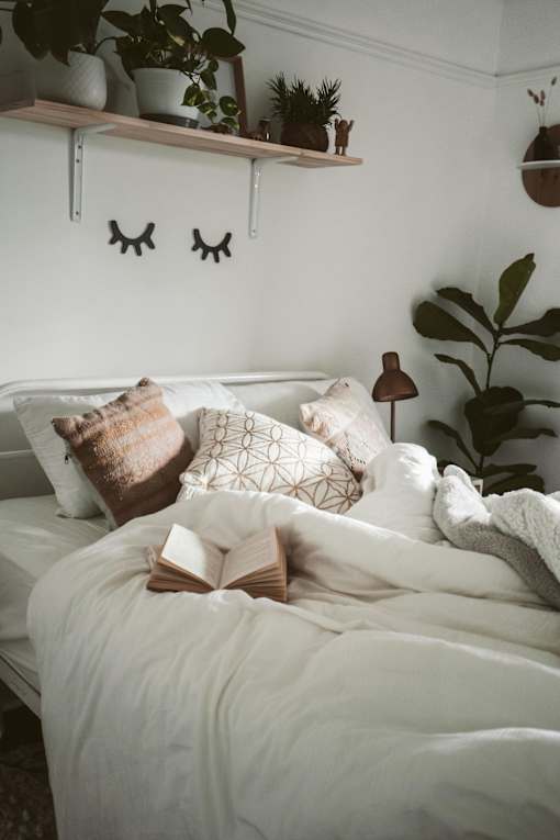 A cozy bedroom with a bed, pillows, a book, and plants.