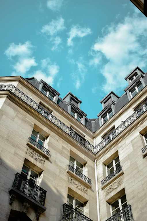 A building with balconies and windows under a blue sky with clouds.
