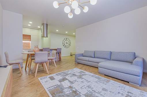 A living room with a grey couch, a dining table with chairs, and a patterned rug.