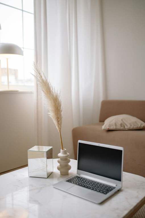 A laptop is on a table with a vase and a lamp in the background.