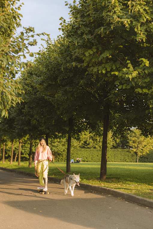 a woman on a skateboard walking her dog in a park