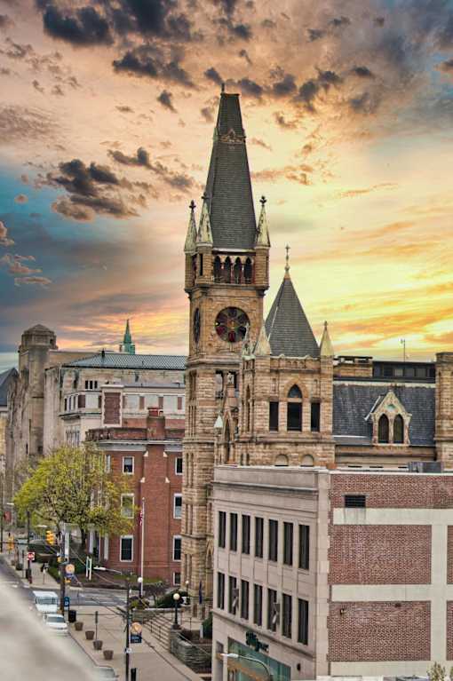 A church steeple rises above a row of buildings in a city.