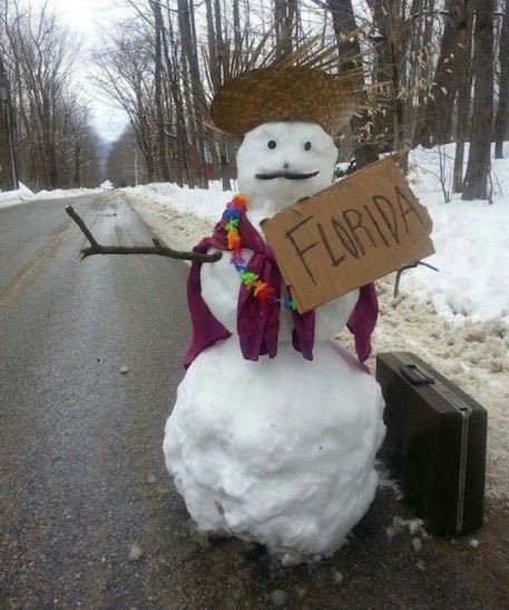a snowman with a straw hat and a suitcase on the side of the road