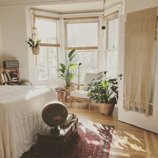 A room with a bed, a chair, a potted plant, and a globe on a table.