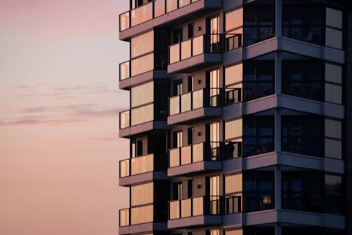 A tall building with balconies is silhouetted against a sunset sky.
