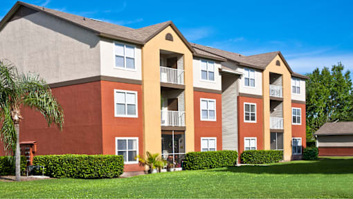 A red and beige apartment building with a green lawn in front.