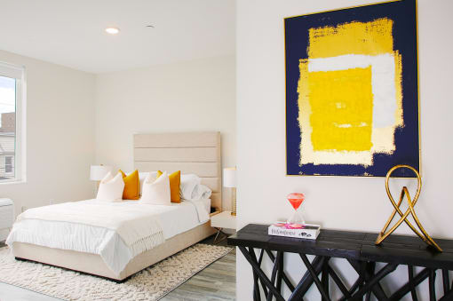 a bedroom with white walls and a large yellow and blue painting on the wall