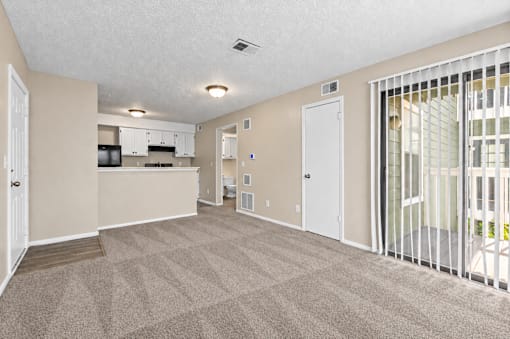 A spacious room with a carpeted floor and a kitchen area in the background.