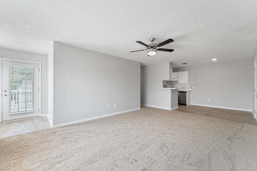 an empty living room with a ceiling fan and a kitchen