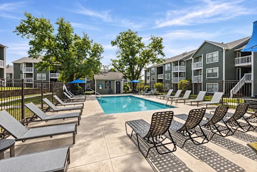A pool surrounded by lounge chairs and trees.