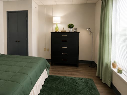A bedroom with a green bedspread and a black dresser.
