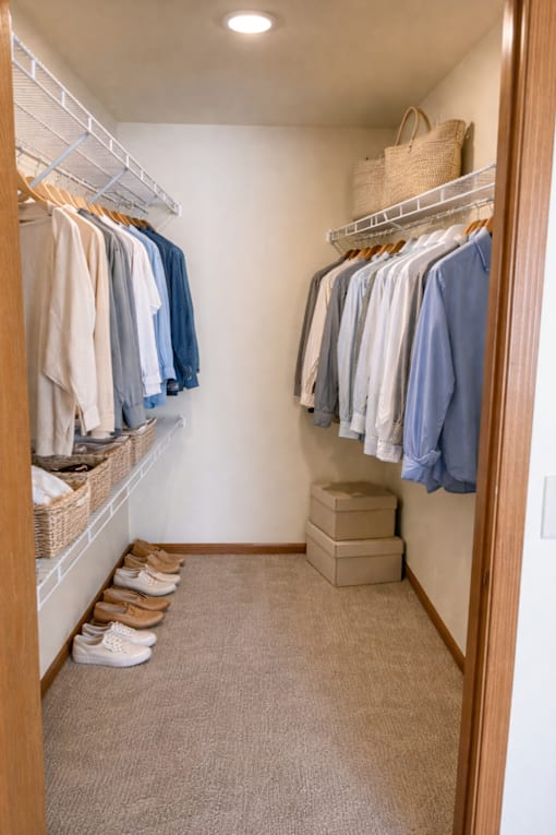 A small closet with clothes hanging and shoes on the floor.